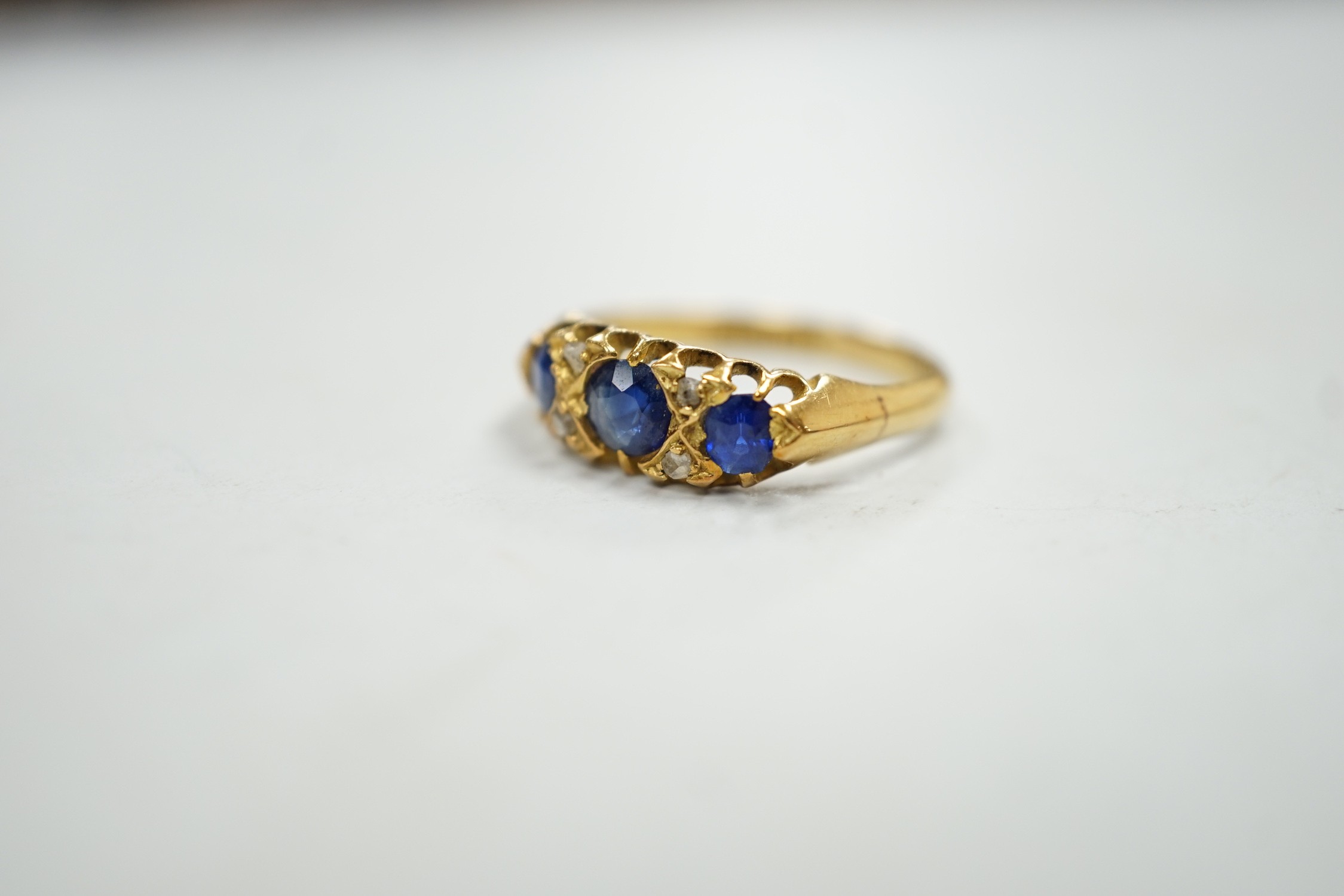 An Edwardian 18ct gold and graduated three stone sapphire set half hoop ring, with four stone rose cut diamond chip spacers, hallmarked for Birmingham, 1906, size P/Q, gross weight 3.2 grams.